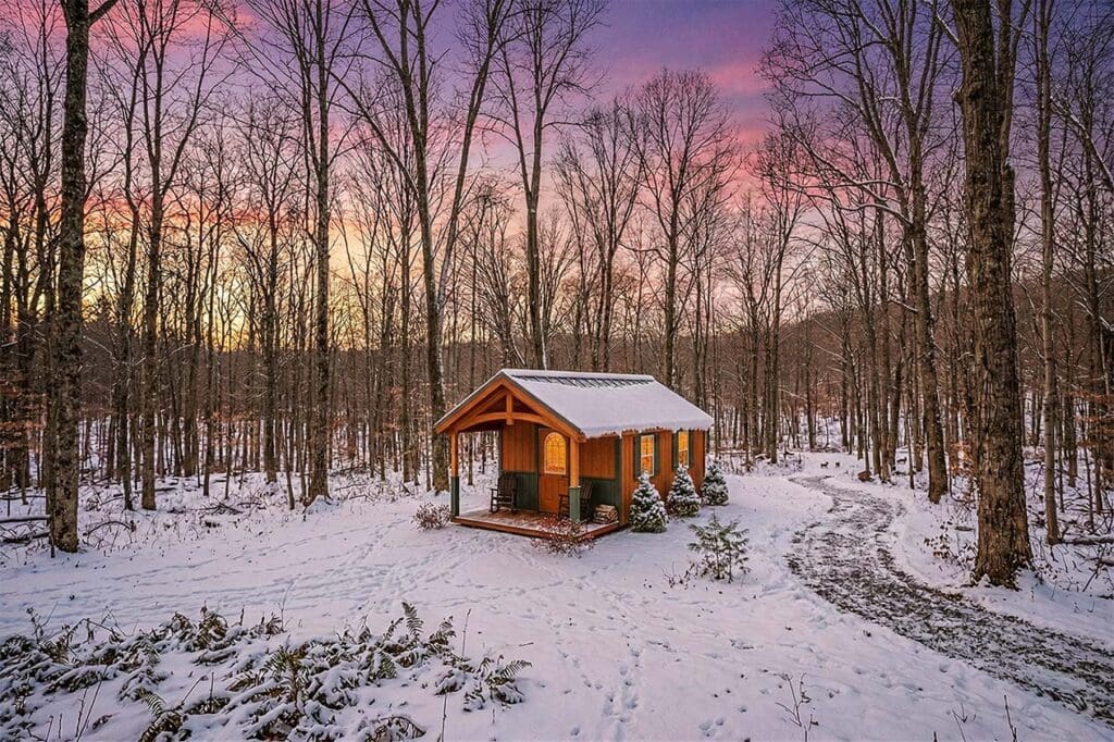 a custom cabin in the woods surrounded by woods and covered in snow. showing the high quality custom cabins by old glory sheds
